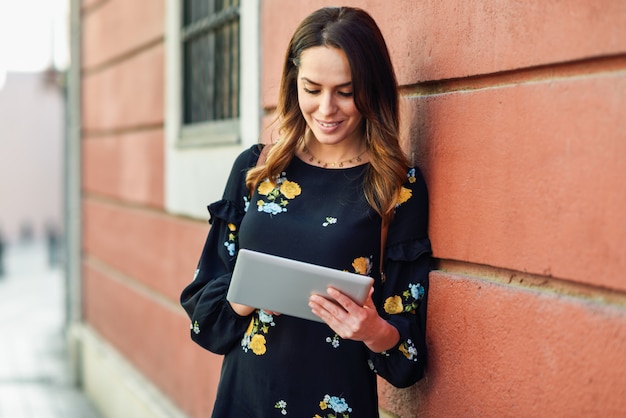 Glimlachende jonge vrouw die digitale tablet in openlucht gebruiken.