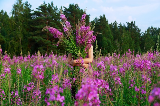 Glimlachende jonge vrouw die een boeket van roze bloemen op een gebied houdt