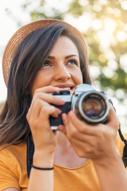 Glimlachende jonge vrouw die een camera gebruikt om foto te nemen bij het park.