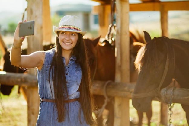 Glimlachende jonge vrouw die een selfie maakt met paarden in de stal.