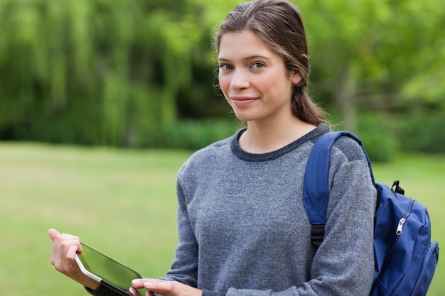 Glimlachende jonge vrouw die een tabletpc houdt terwijl status in een park