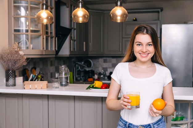 Glimlachende jonge vrouw die glas jus d'orange en sinaasappel toont