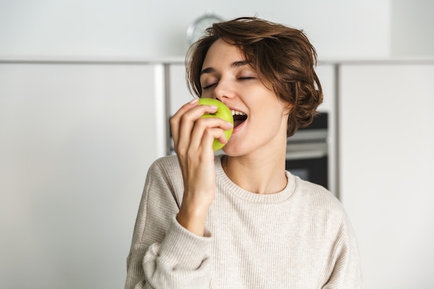 Glimlachende jonge vrouw die groene appel houdt bij de keuken
