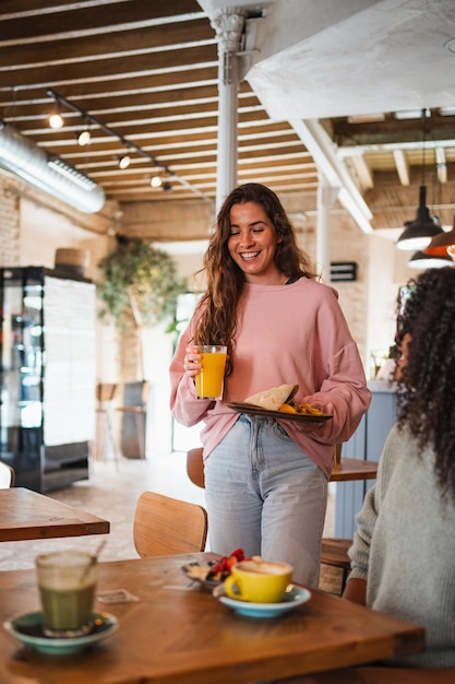 Foto glimlachende jonge vrouw die haar eten naar de tafel brengt in een brunchrestaurant