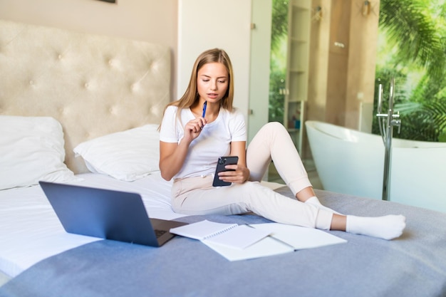 Glimlachende jonge vrouw die haar rekeningen online betaalt met laptop in slaapkamer thuis