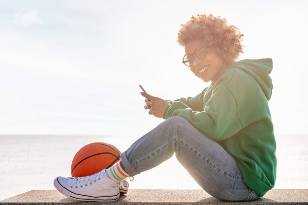 Glimlachende jonge vrouw die haar telefoon gebruikt bij zonsondergang