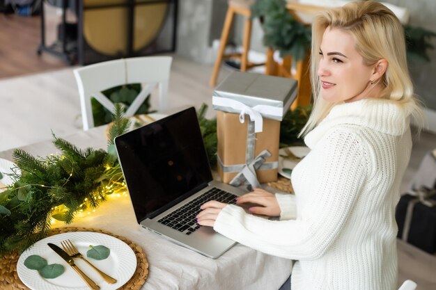 Glimlachende jonge vrouw die laptop met behulp van in de buurt van kerstboom.