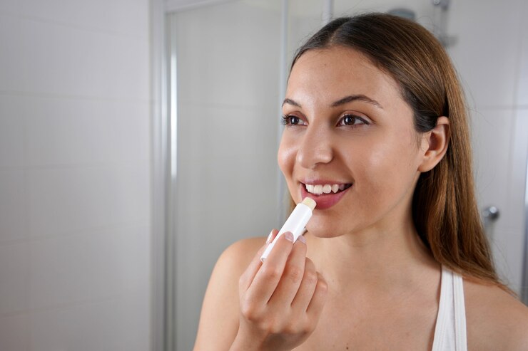Glimlachende jonge vrouw die lippenbalsem voor de spiegel binnen toepast
