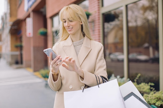 Glimlachende jonge vrouw die met haar mobiele telefoon winkelt in de stad