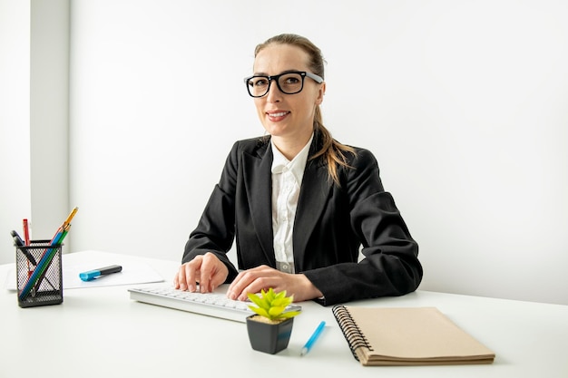 Glimlachende jonge vrouw die op het toetsenbord typt terwijl ze aan het bureau zit op de werkplek