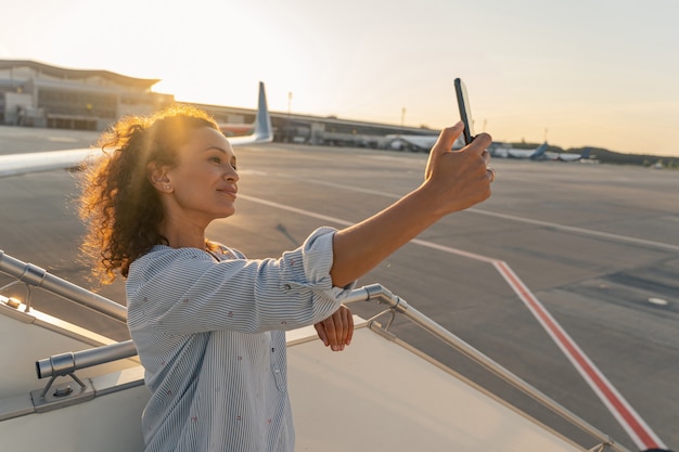 Glimlachende jonge vrouw die selfie op smartphone in luchthaven maakt