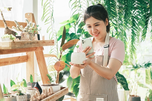 Glimlachende jonge vrouw die smartphonefoto maakt van een plant in een kleine winkel