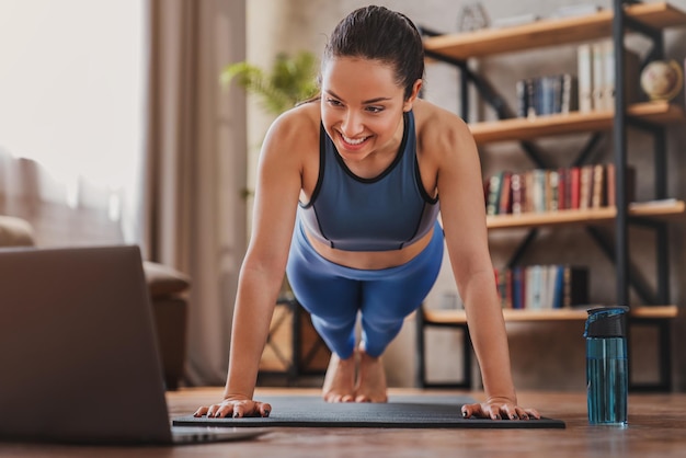 Glimlachende jonge vrouw die trainingsvideo's op laptop bekijkt terwijl ze thuis traint