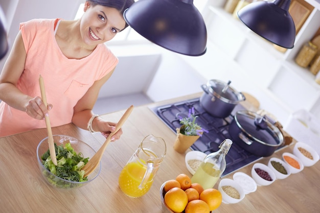 Foto glimlachende jonge vrouw die verse salade in de keuken mengt