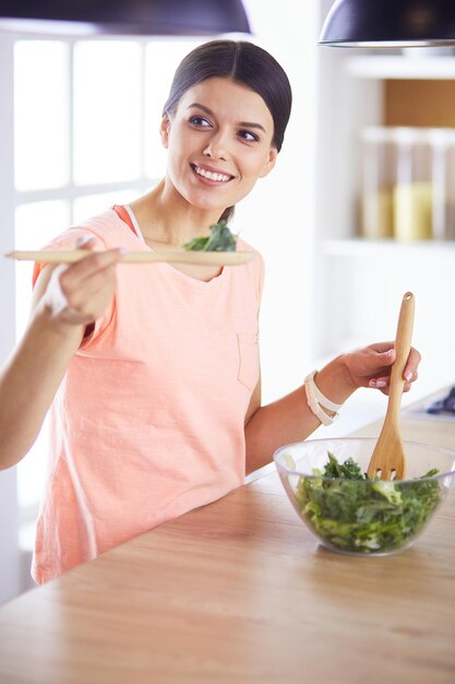 Glimlachende jonge vrouw die verse salade in de keuken mengt