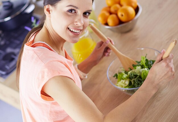 Glimlachende jonge vrouw die verse salade in de keuken mengt