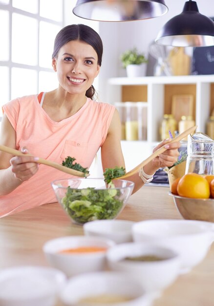 Glimlachende jonge vrouw die verse salade in de keuken mengt