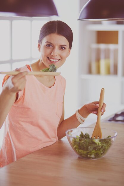 Glimlachende jonge vrouw die verse salade in de keuken mengt