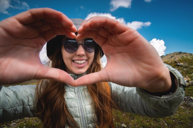 Glimlachende jonge vrouw die vingers toont gebaar teken van hart liefde in de bergen gelukkige toerist