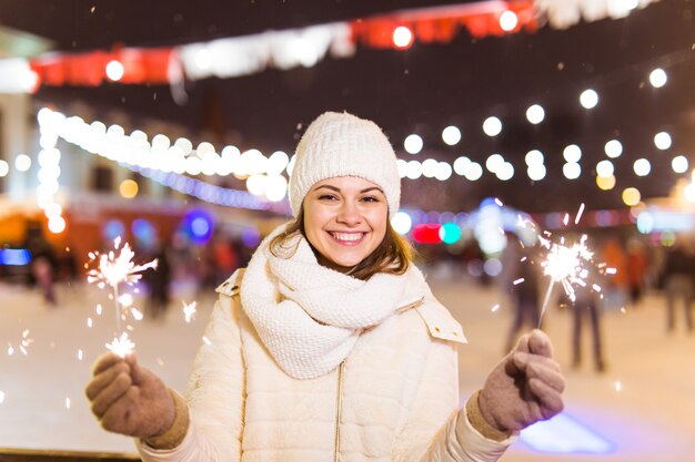 Foto glimlachende jonge vrouw die wintergebreide kleding draagt die sterretje buiten over sneeuwachtergrond houdt