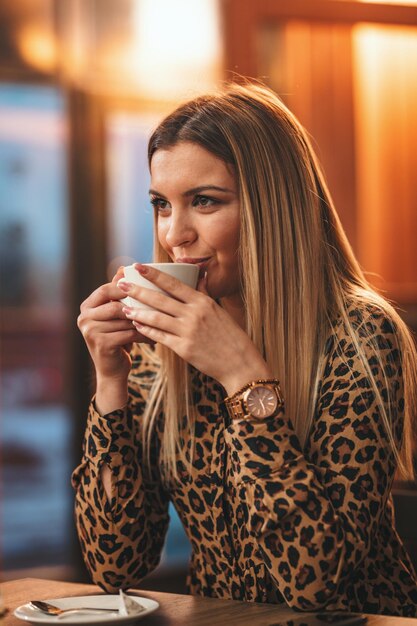 Glimlachende jonge vrouw drinkt koffie terwijl ze in het café zit.