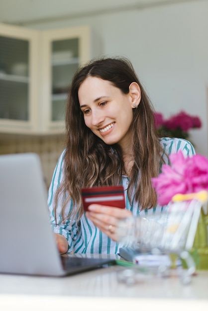 Glimlachende jonge vrouw gebruikend creditcard en online koopend iets