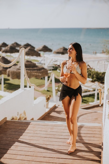 Glimlachende jonge vrouw in bikini geniet van een vakantie op het strand terwijl ze een cocktail drinkt