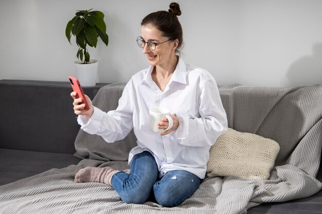 Glimlachende jonge vrouw in bril met telefoon praten over videolink zittend op de bank