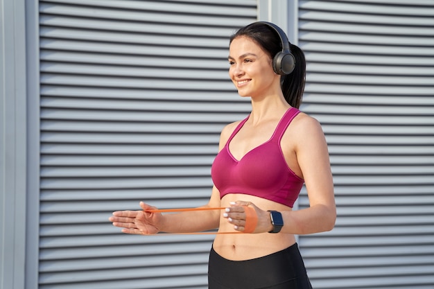 Glimlachende jonge vrouw in draadloze koptelefoon met behulp van fitness elastiekjes. Sportconcept. Ruimte kopiëren