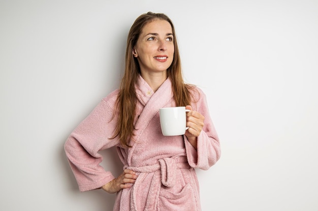 Glimlachende jonge vrouw in een badjas met een kopje op een witte achtergrond