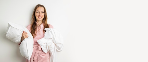 Glimlachende jonge vrouw in een badjas met een kussen en een laken op een witte achtergrond banner