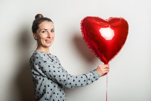 Glimlachende jonge vrouw in een trui met een hart-luchtballon op een lichte achtergrond. valentijnsdag concept. banner.