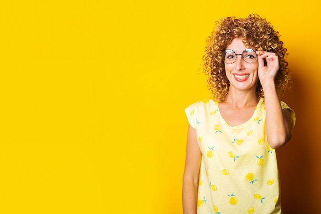 Glimlachende jonge vrouw in ronde transparante bril op een gele achtergrond.