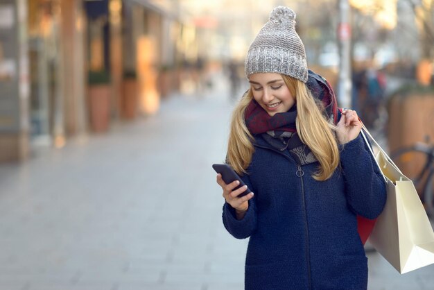Glimlachende jonge vrouw met blond haar die telefoon gebruikt op de stoep