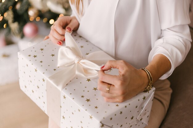 Glimlachende jonge vrouw met de huidige doos van Kerstmis dichtbij de kerstboom