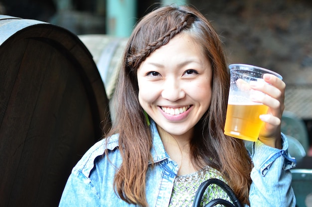 Foto glimlachende jonge vrouw met een bierglas tegen vaten op een zonnige dag