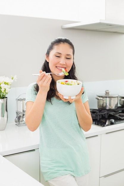 Glimlachende jonge vrouw met een kom salade in keuken