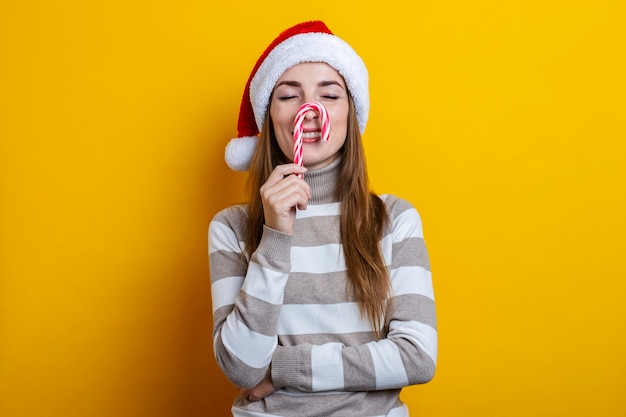 Glimlachende jonge vrouw met gesloten ogen met kerstsnoep op haar neus tegen gele achtergrond.