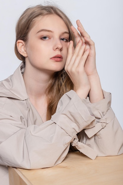 Glimlachende jonge vrouw met glas water mooi meisje in beige regenjas poseren in studio