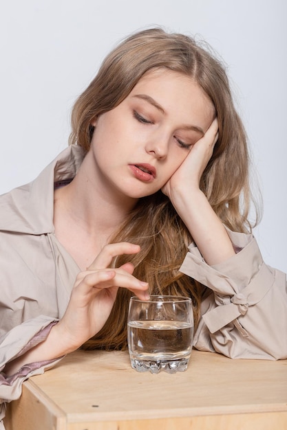 Glimlachende jonge vrouw met glas water mooi meisje in beige regenjas poseren in Studio