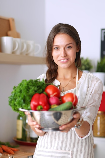 Glimlachende jonge vrouw met groenten die in de keuken staan Glimlachende jonge vrouw