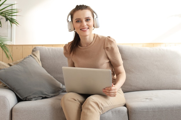 Glimlachende jonge vrouw met koptelefoon en laptop op de bank.