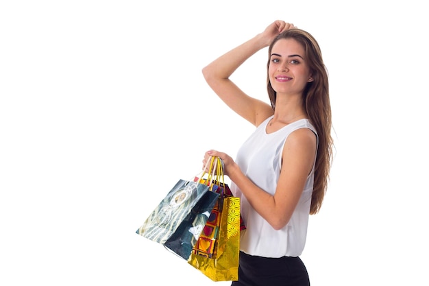 Glimlachende jonge vrouw met lang haar in witte blouse en zwarte rok met boodschappentassen in studio