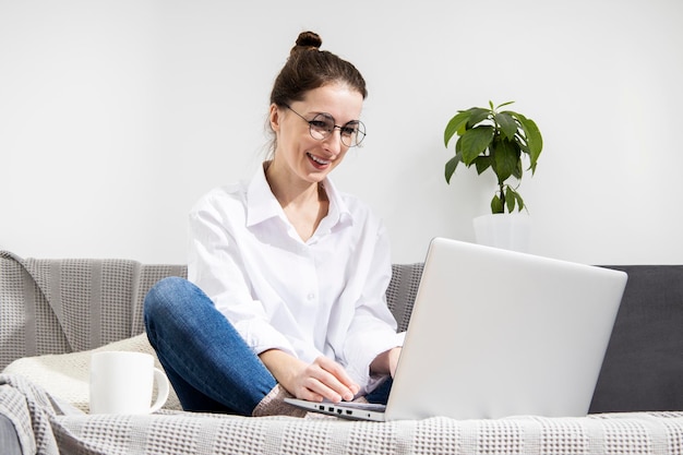 Glimlachende jonge vrouw met laptop met koffie zittend op de bank