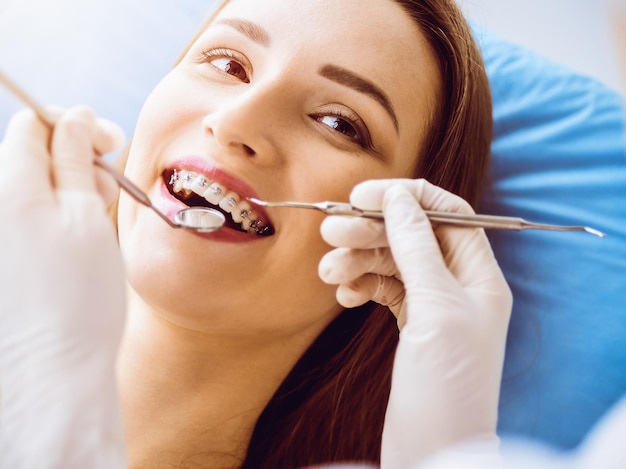 Glimlachende jonge vrouw met orthodontische beugels onderzocht door tandarts in zonnige tandheelkundige kliniek Gezonde tanden en geneeskunde concept