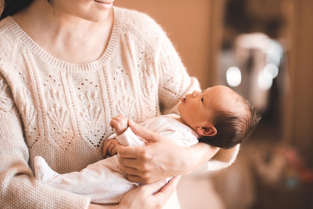 Glimlachende jonge vrouw met schattige kleine baby van 12 maanden oud op haar handen in de kamer thuis close-up Moederschap Gezonde levensstijl