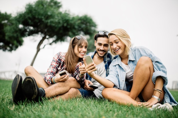 Glimlachende jonge vrouw met vrienden die telefoon gebruiken op het veld