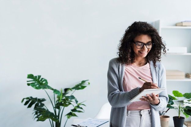 Glimlachende jonge vrouw schrijft in een krabbelblok op de werkplek