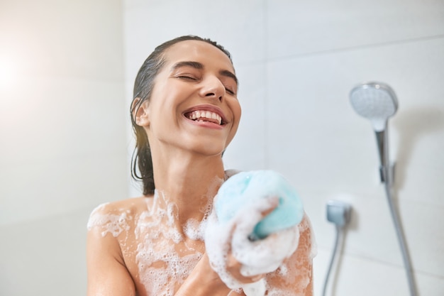 Glimlachende jonge vrouw wassen lichaam met bad luffa