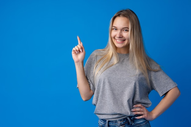 Glimlachende jonge vrouw wijzend op kopieerruimte over blauwe achtergrond